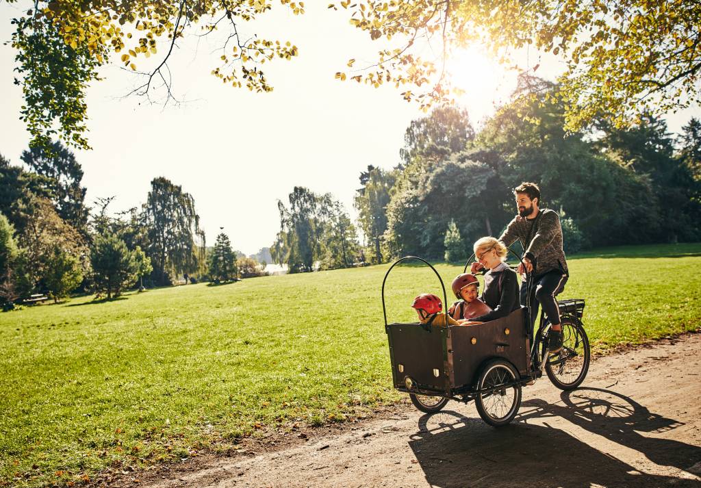 Een vader en moeder die samen met hun twee kinderen aan het fietsen zijn in een park met een bakfiets