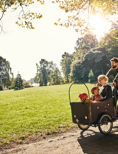 Een vader en moeder die samen met hun twee kinderen aan het fietsen zijn in een park met een bakfiets
