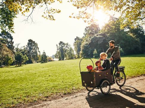 Een vader en moeder die samen met hun twee kinderen aan het fietsen zijn in een park met een bakfiets